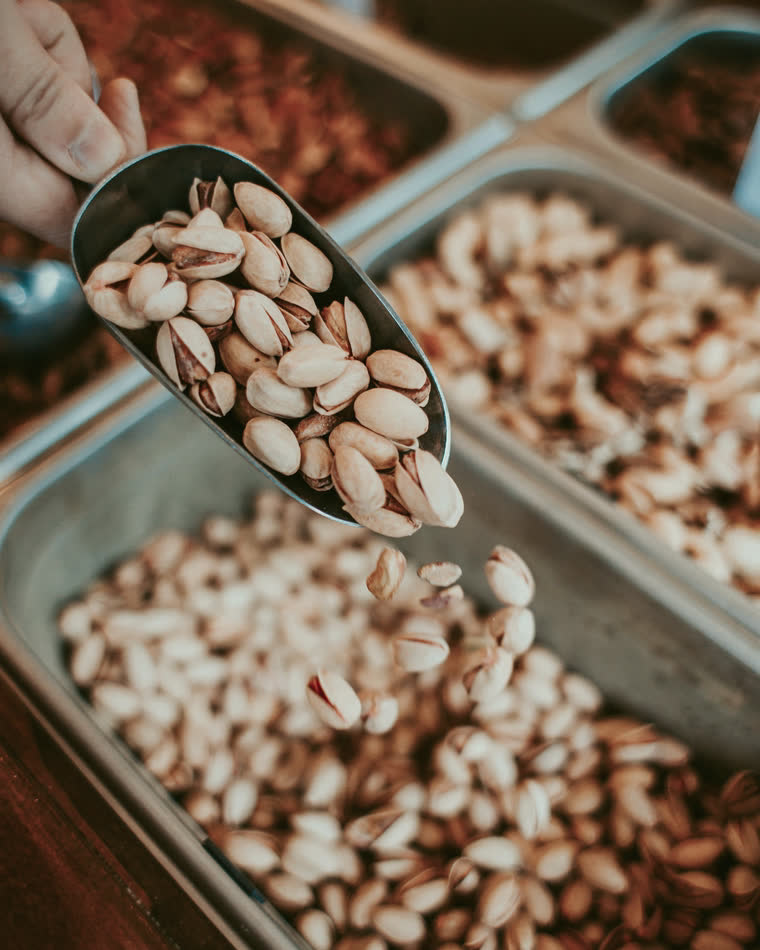 A scoop pouring pistachios into a bin.